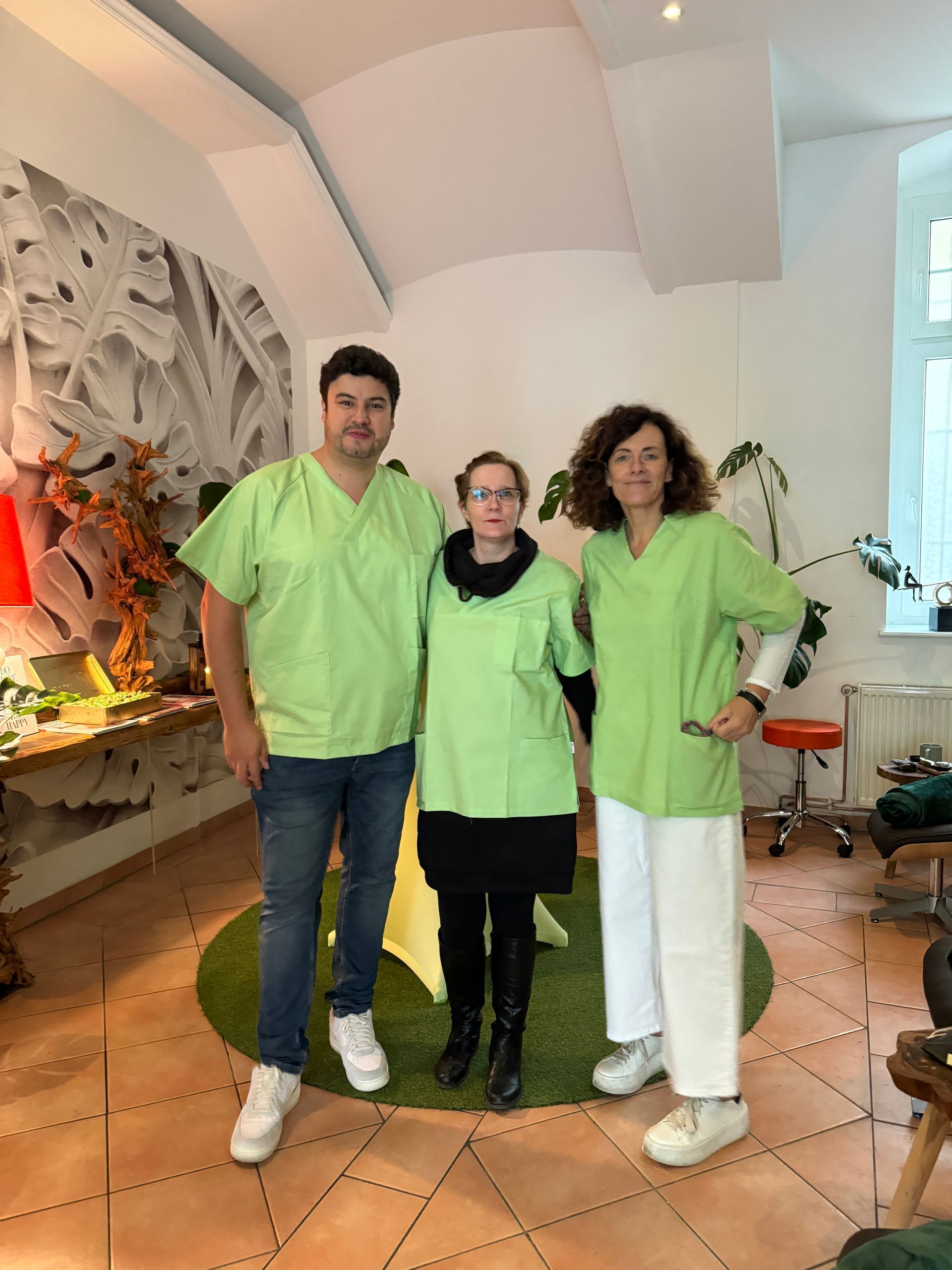 Drei Menschen in grünen Kitteln posieren in einem Raum für ein Foto.