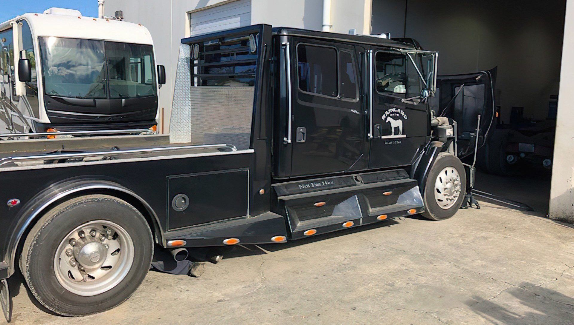 Black tow truck with an extended cab parked in front of a building.