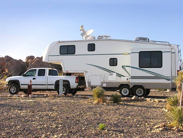 White truck towing a large fifth-wheel RV in a rocky desert area.