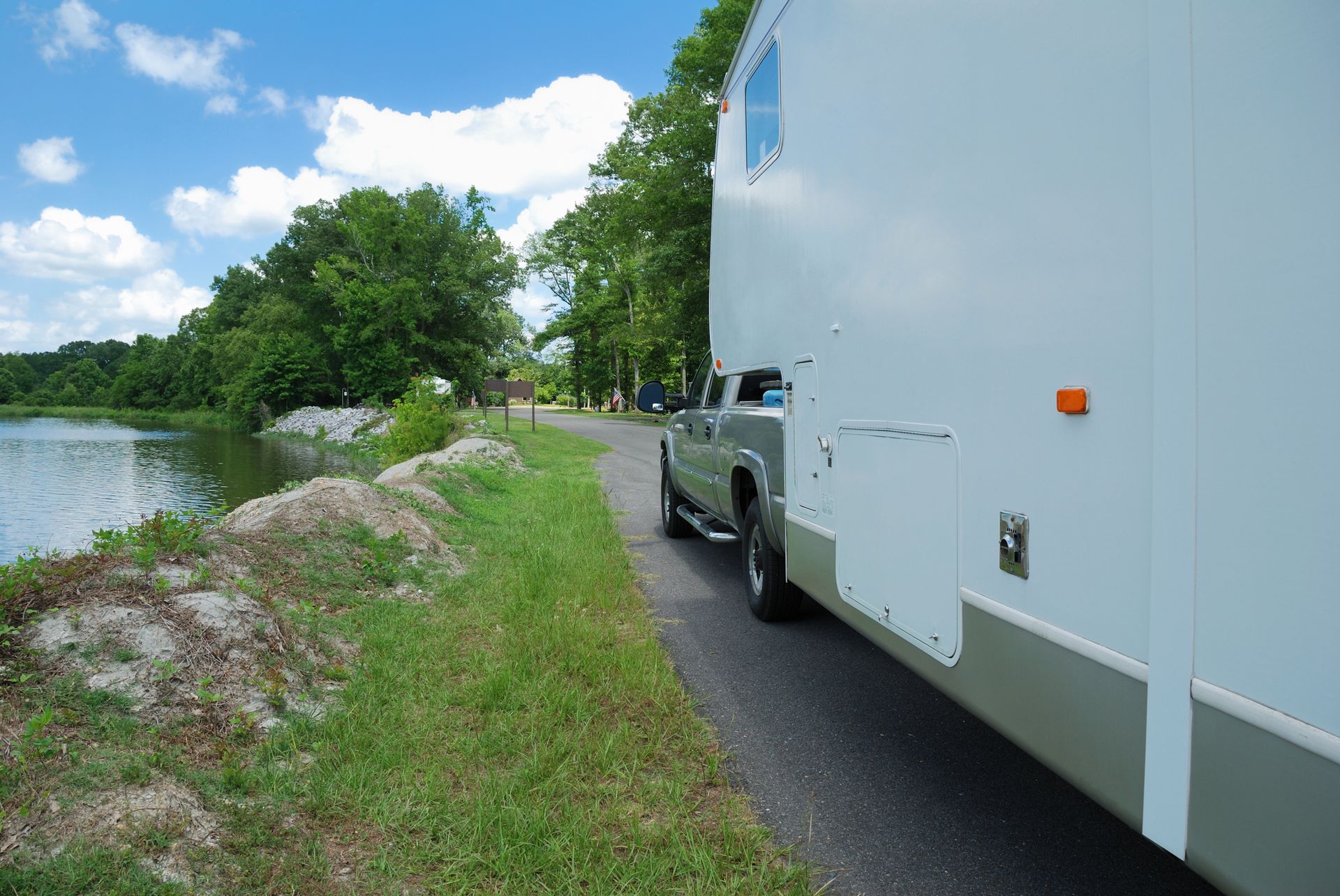 Fifth-wheel trailer and truck parked near river.