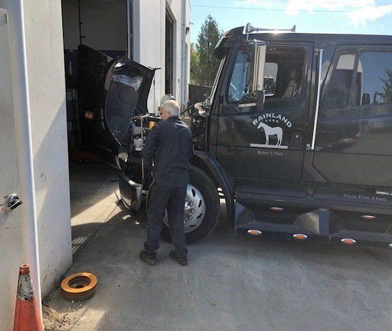 Mechanic working on the engine of a black semi-truck parked outside a garage with 