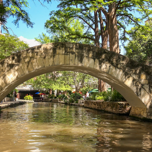 Stone arch bridge over a river, lined with trees and greenery; sunny day.
