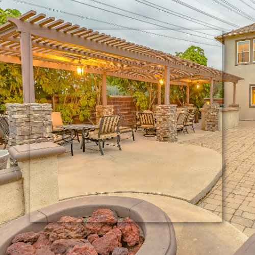 Patio with pergola, seating, and fire pit in a backyard with a house in the background.