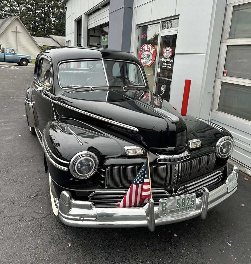 A black car with an american flag on the front is parked in front of a building