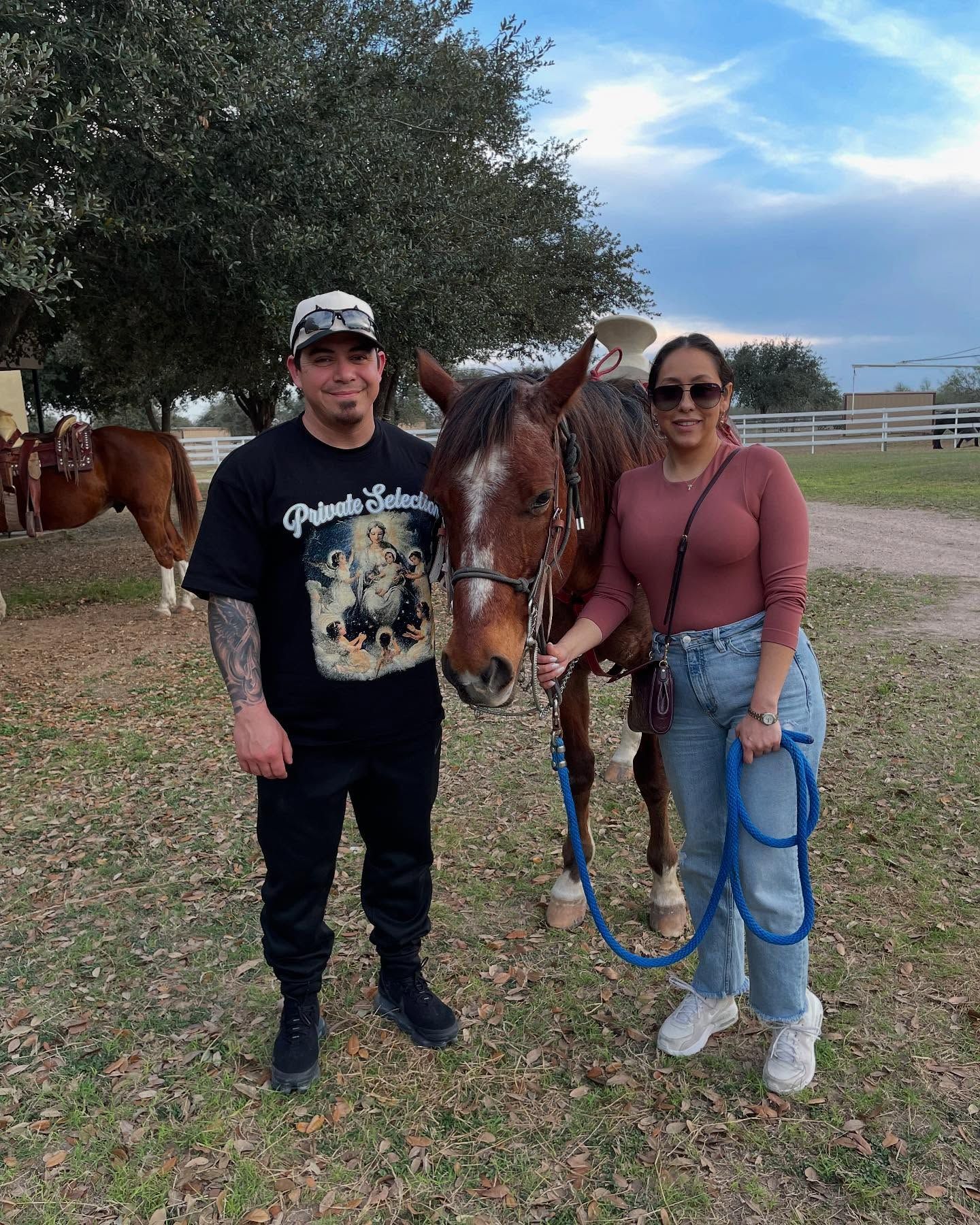Man and woman pose with a brown horse in an outdoor field setting.