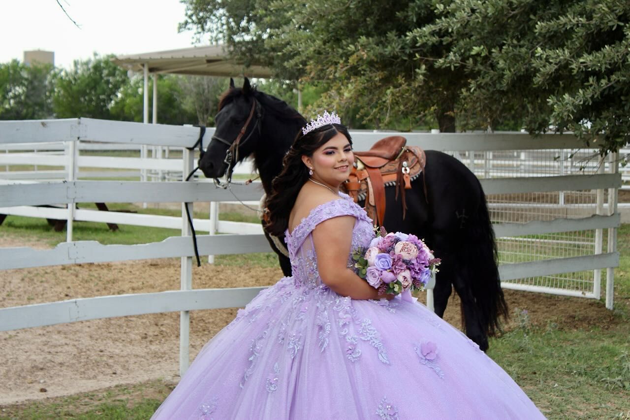 Woman in lavender gown with horse, posing by a white fence. She wears a crown and holds flowers.