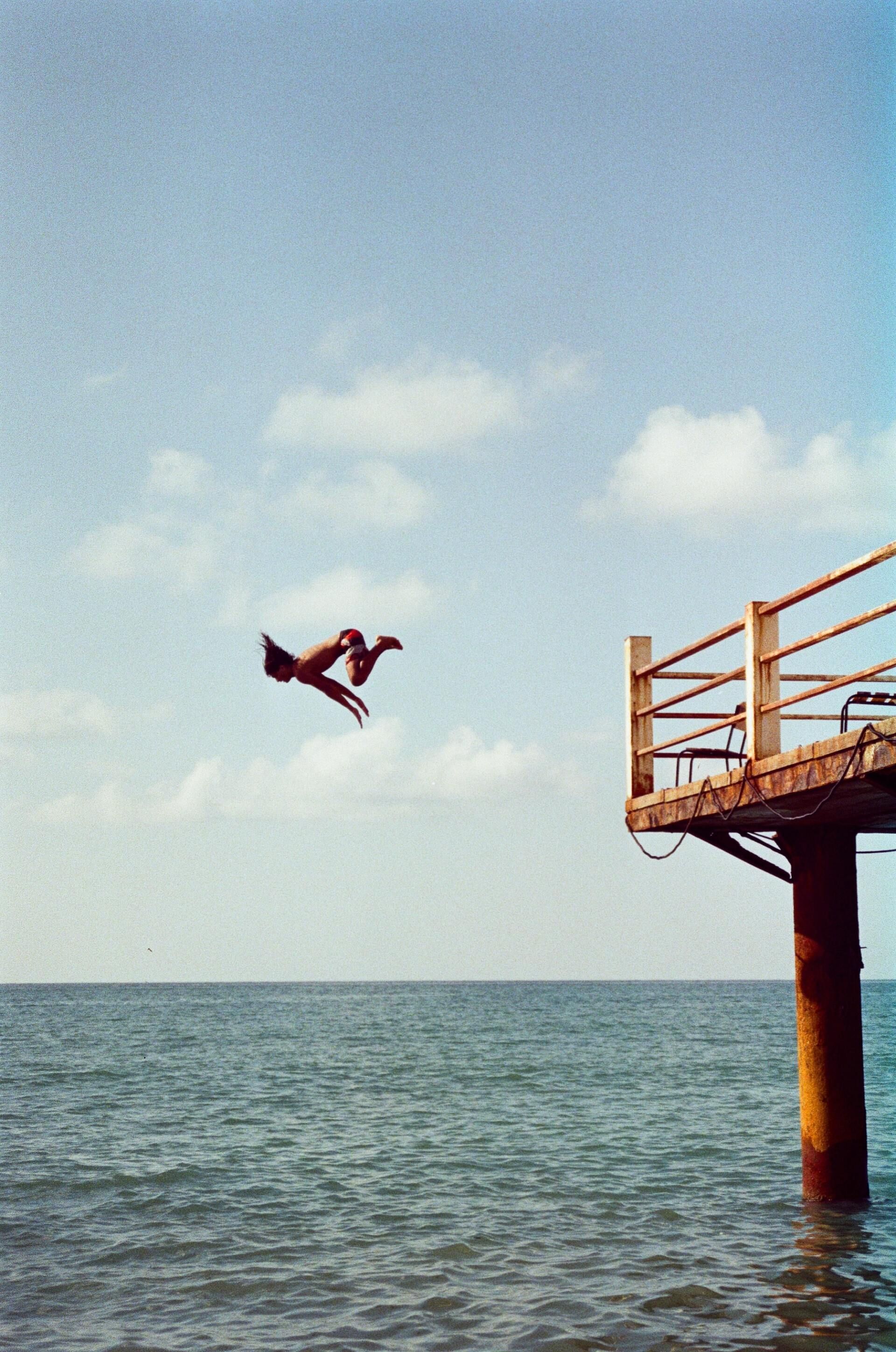 A person is jumping off a pier into the ocean