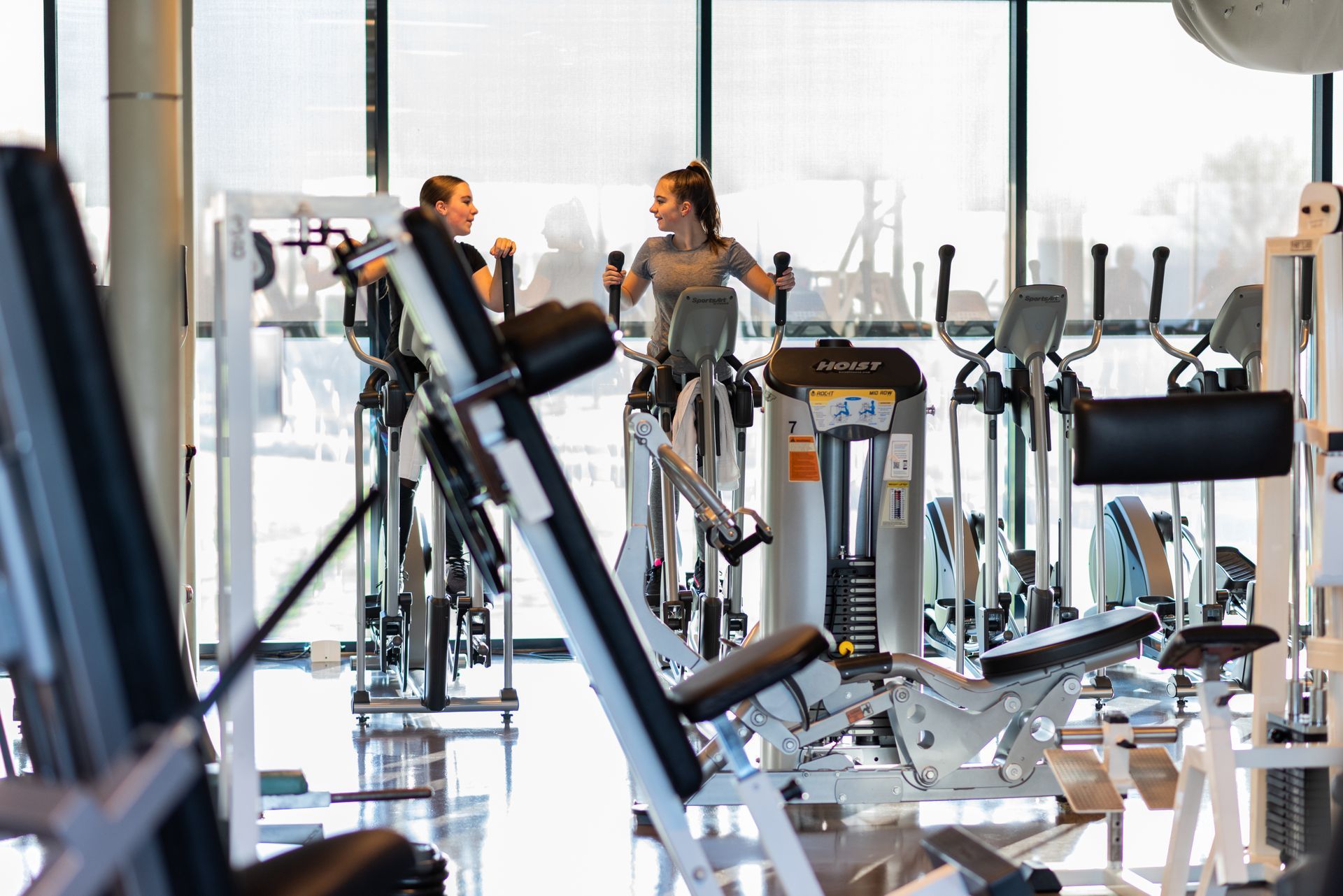 Twee vrouwen fietsen op hometrainers in een sportschool.