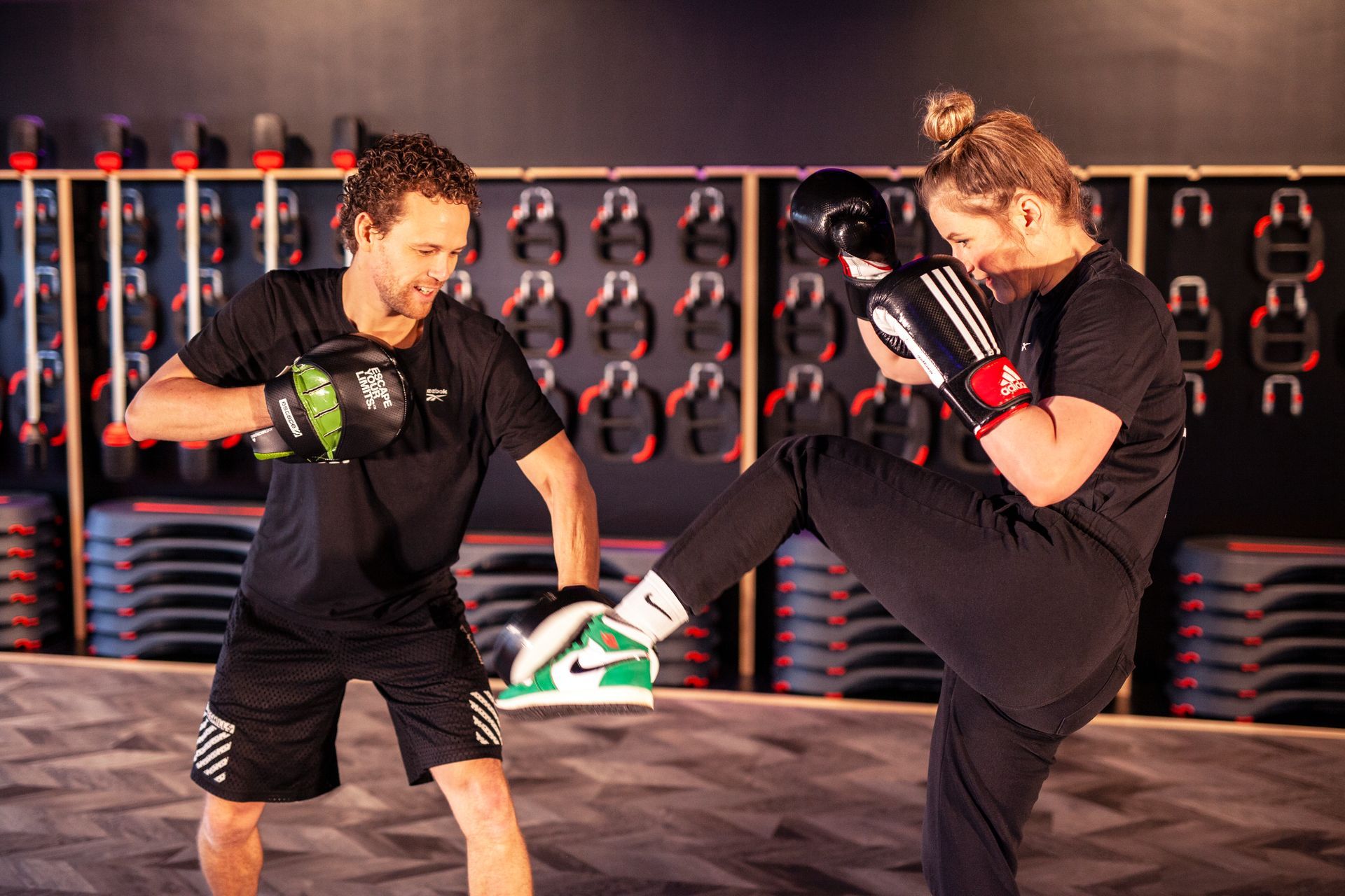 Man and woman training crossboxing in a gym. Man holds pads, woman kicks.