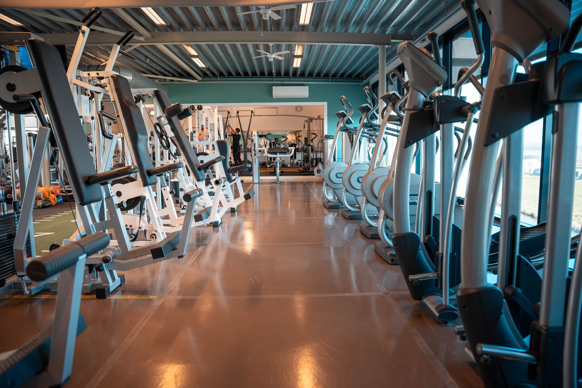 Een sportschool vol met fitnessapparatuur en een houten vloer.