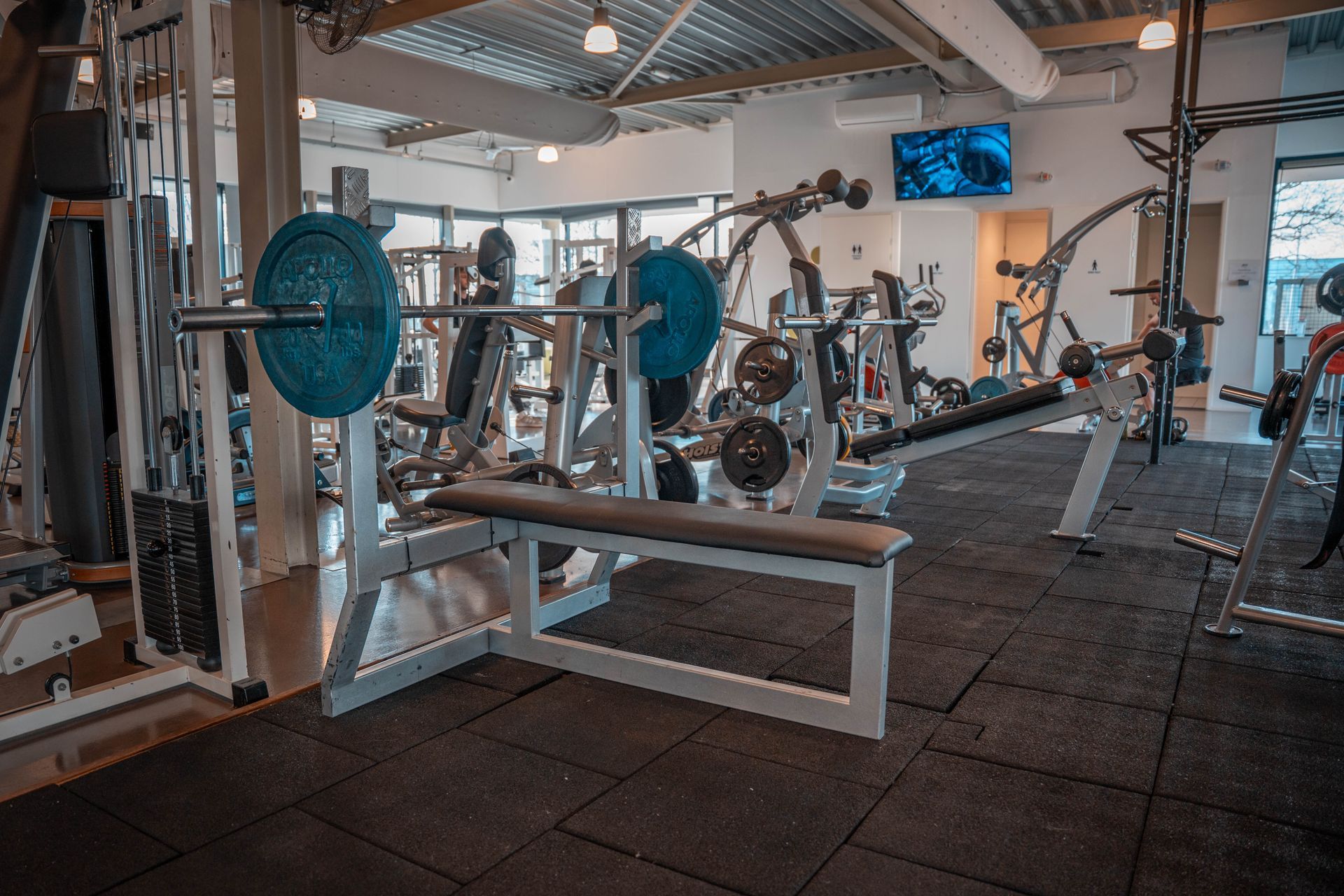 Een sportschool vol met fitnessapparatuur en een bank met een halterstang erop.