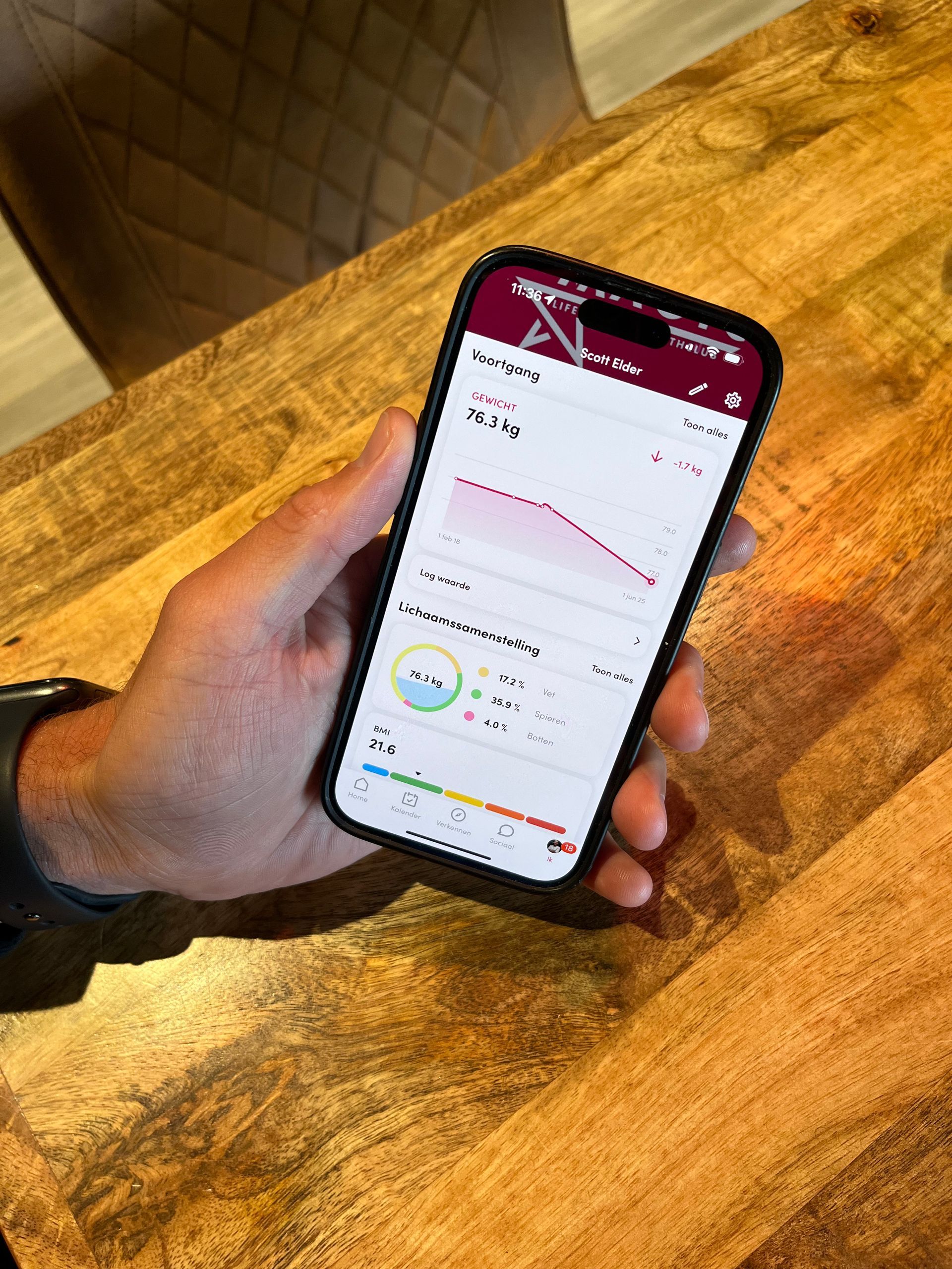 Een persoon houdt een mobiele telefoon in zijn hand op een houten tafel.