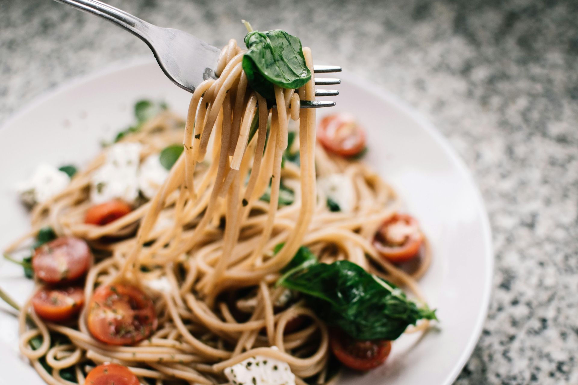 Fork of spaghetti pasta with cherry tomatoes, basil, and cheese on a white plate.