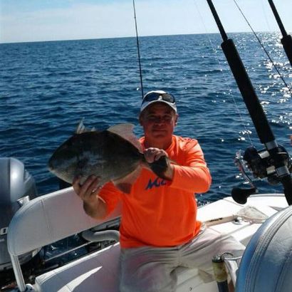 A man in an orange shirt is holding a fish on a boat