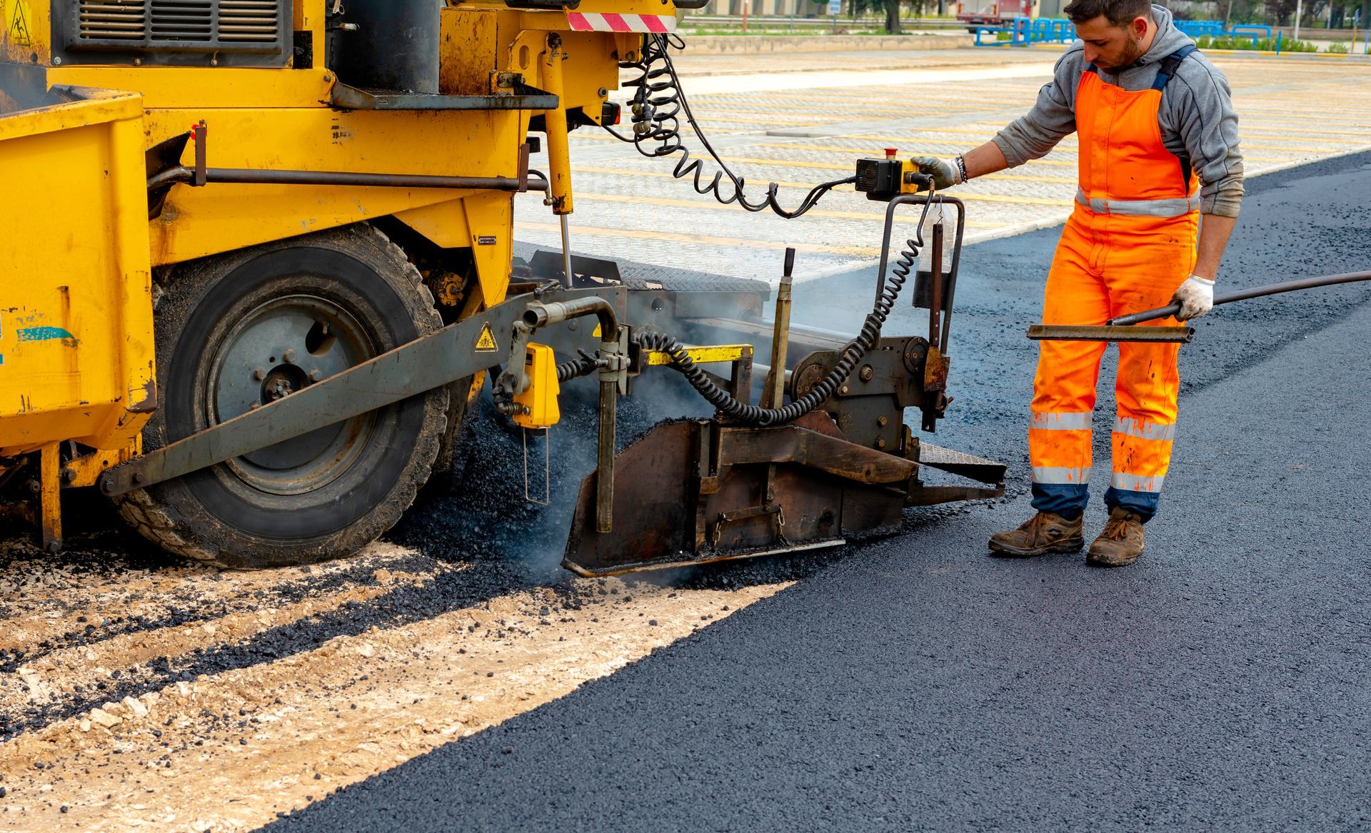 Yellow asphalt milling machine, operator in orange safety gear, on road, preparing surface.