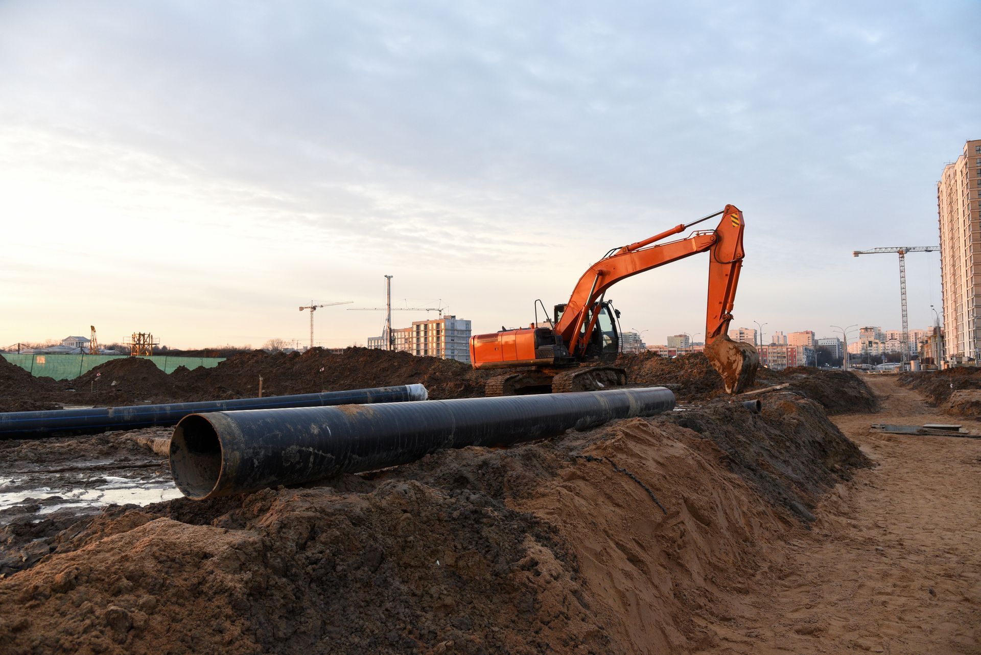 Orange excavator digging near black pipes on a construction site.