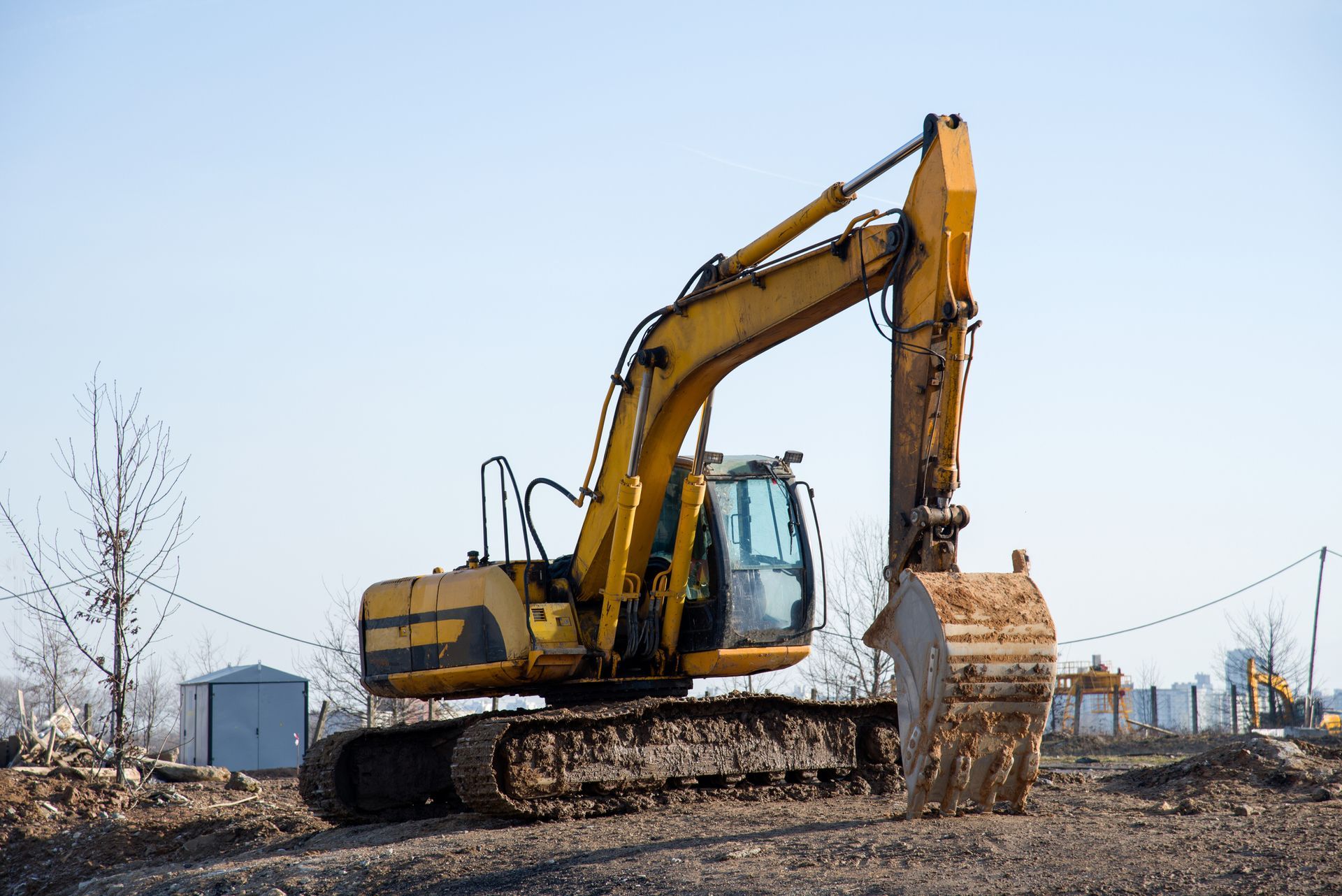 Yellow excavator on a construction site, bucket down, against a clear sky.