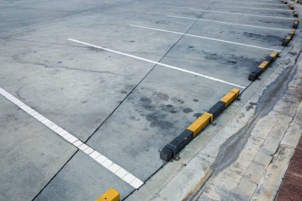 Empty parking lot with white lines and black and yellow curb stops along a concrete edge.