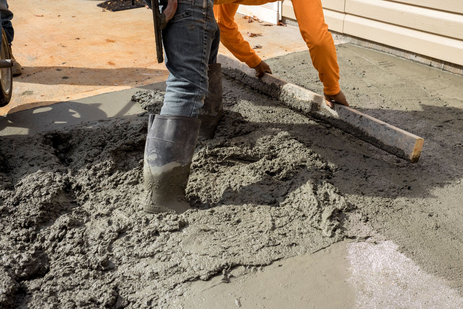 Construction worker smoothing wet concrete with a long wooden tool.
