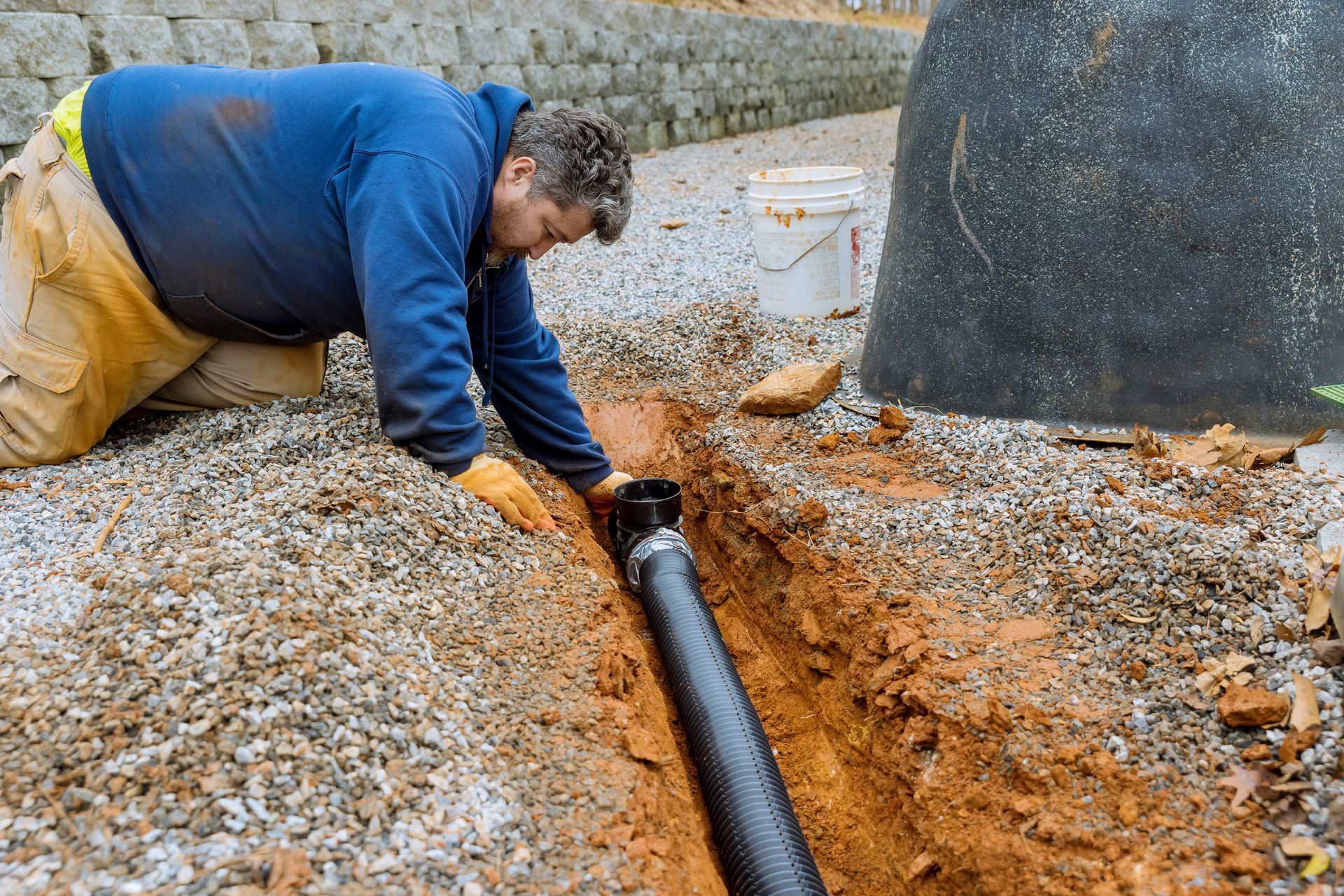 Man installing perforated pipe in a trench filled with gravel.