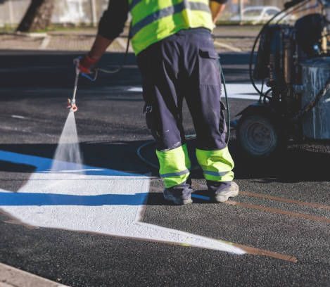 Road worker paints white lines on asphalt with a spray gun, wearing a reflective vest. Road worker paints white lines on asphalt with a spray gun, wearing a reflective vest.
