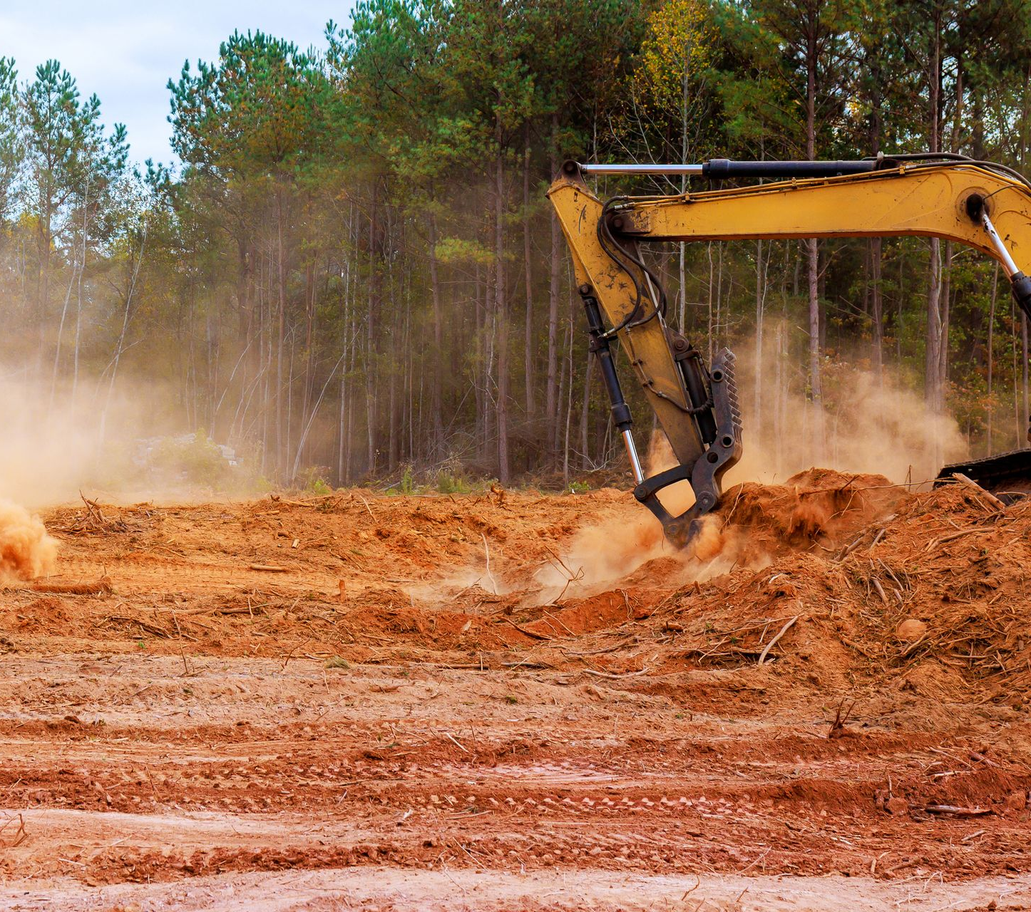 Yellow excavator clearing land, kicking up dust; forest in the background. Yellow excavator clearing land, kicking up dust; forest in the background.