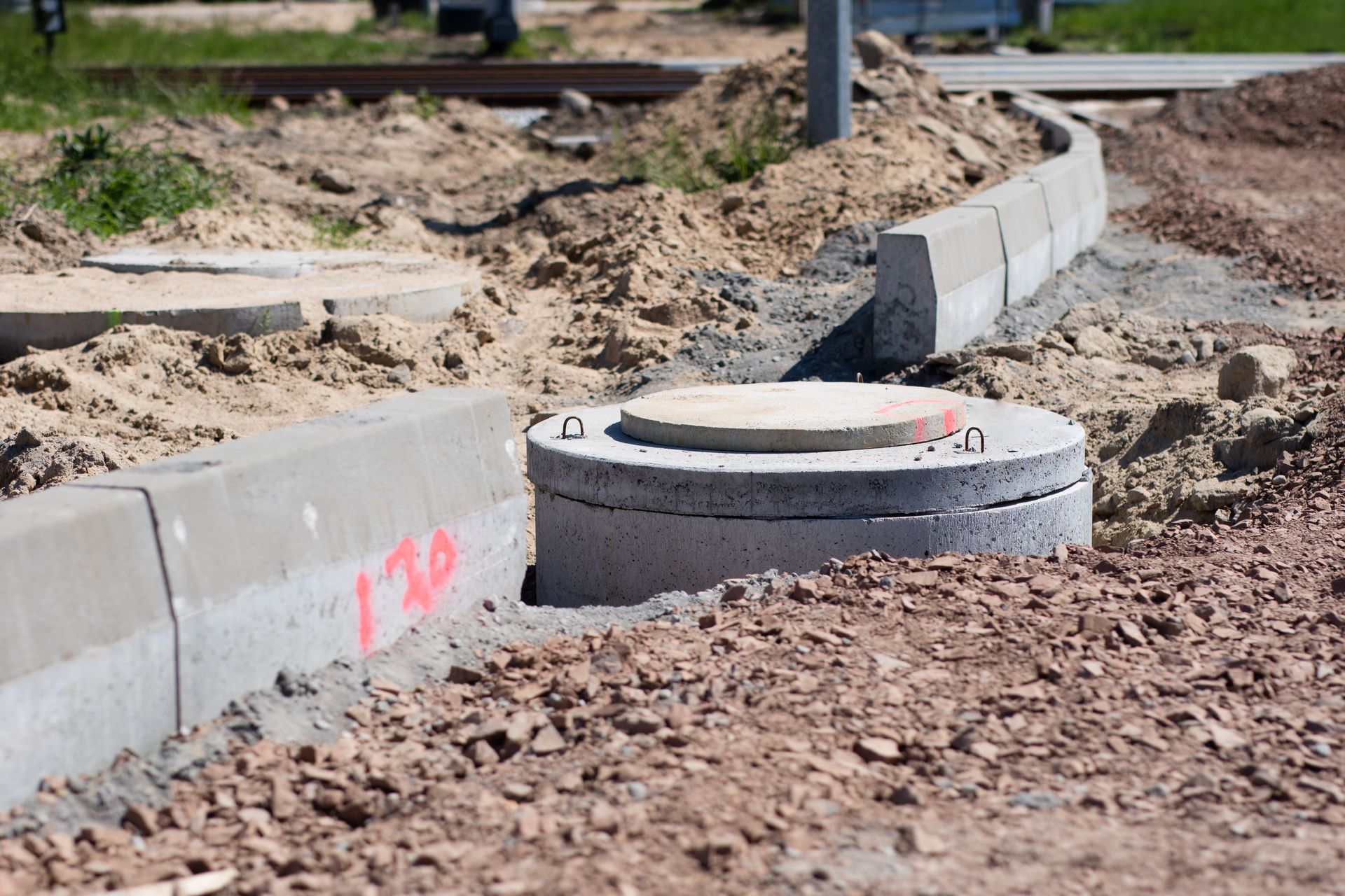 Construction site: Concrete curb, manhole, and gravel.
