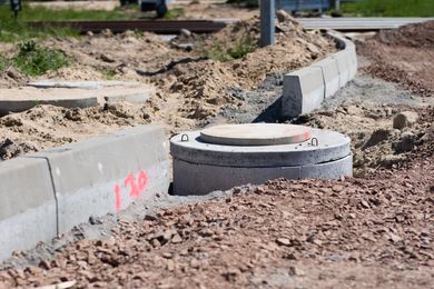 Construction site: Concrete curb, manhole, and gravel.