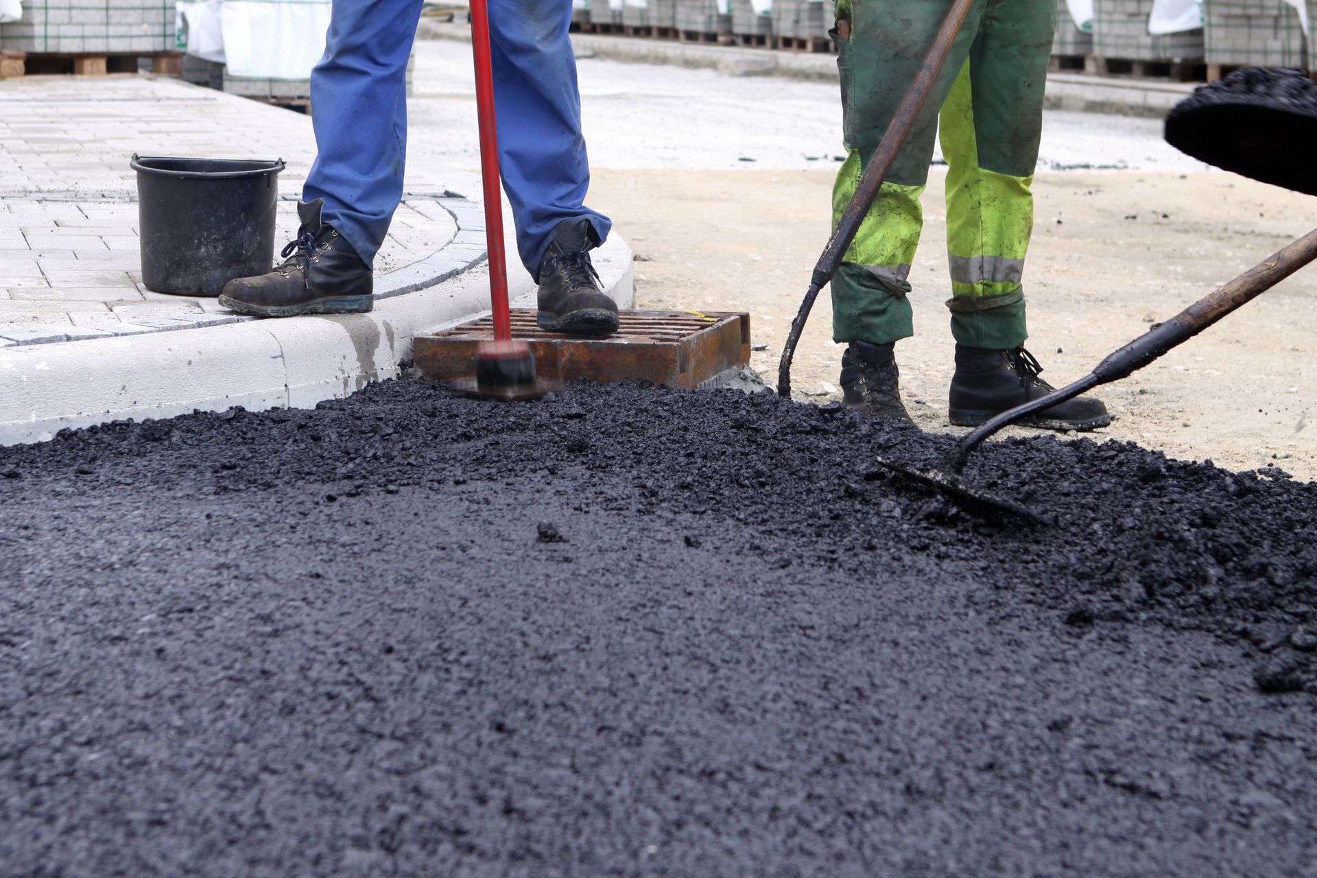 Road workers laying asphalt on a street using rakes and tools.
