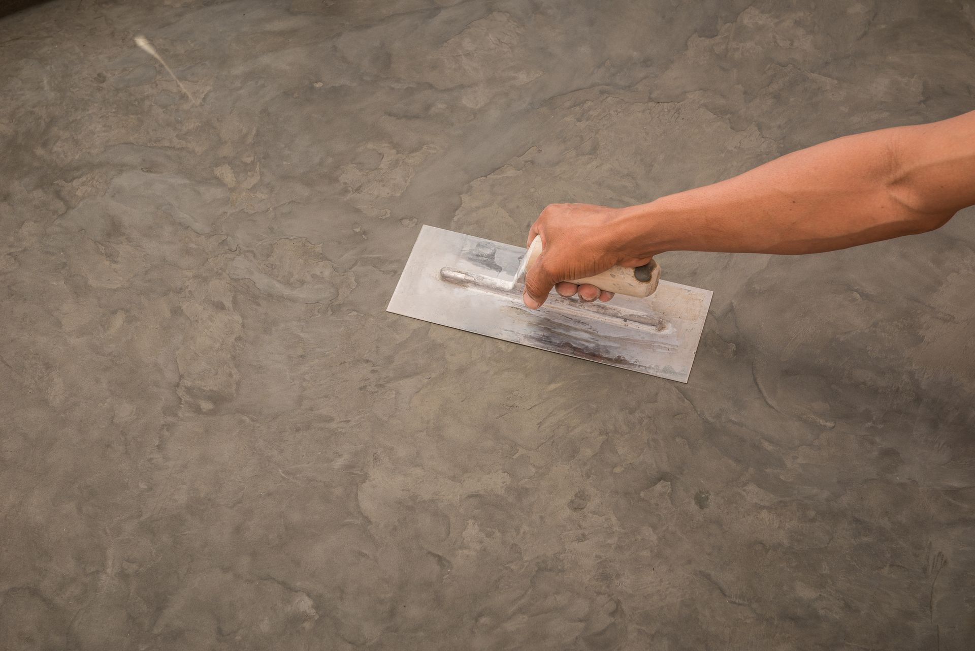 Hand using a trowel to smooth a gray concrete surface.