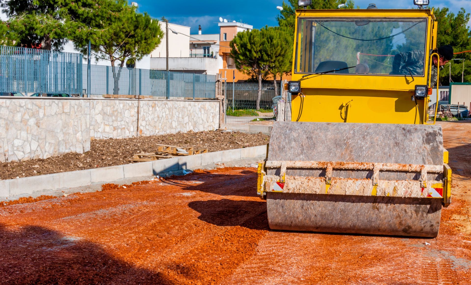 Yellow road roller compacting red soil at a construction site.