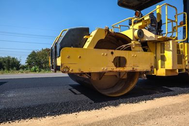 Yellow road roller compacting fresh asphalt on a road, blue sky background.