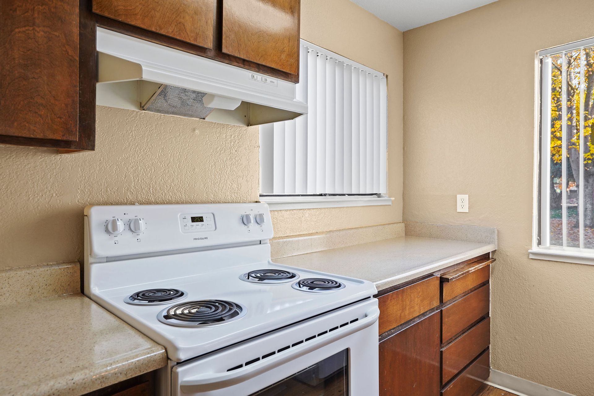 Small beige kitchen with white stove, countertop, cabinets, and a window.