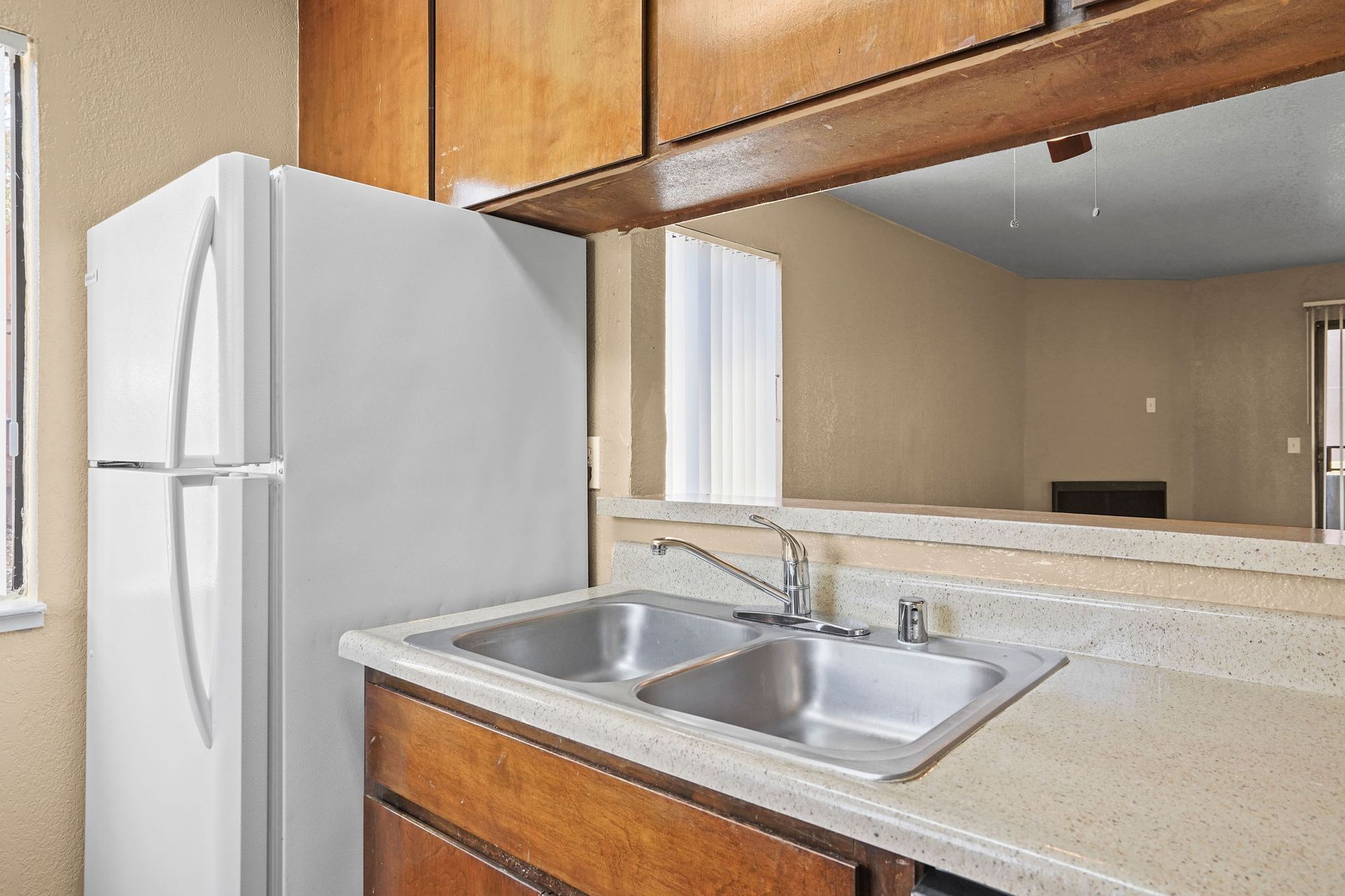 Kitchen with white refrigerator, double sink, beige countertops, and wood cabinets with a mirror backsplash