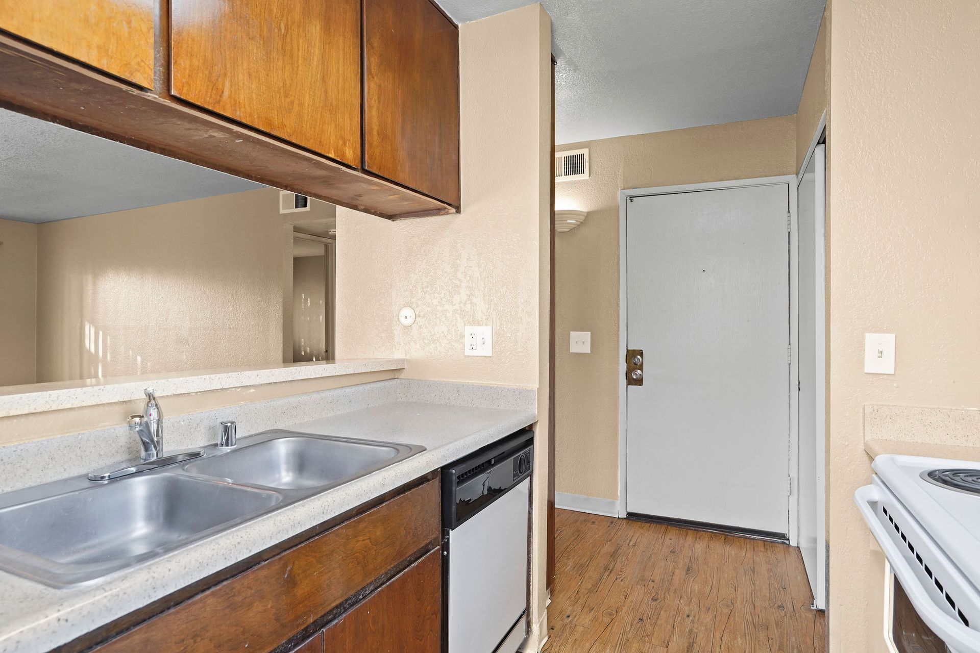 Small kitchen with wood cabinets, double sink, dishwasher, and a view of the front door.