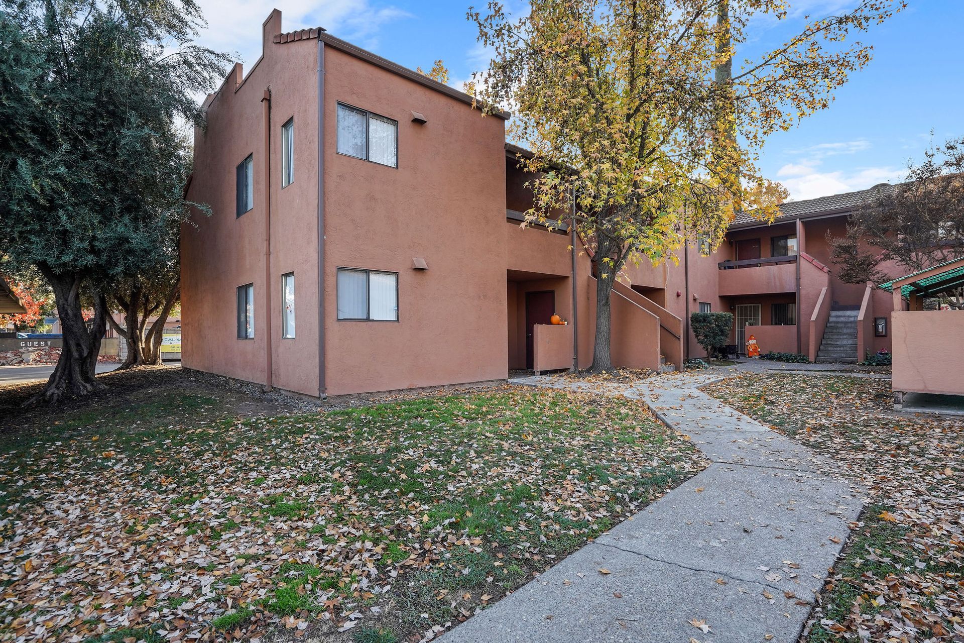 Apartment building with a curved sidewalk, grass, and trees in a courtyard setting