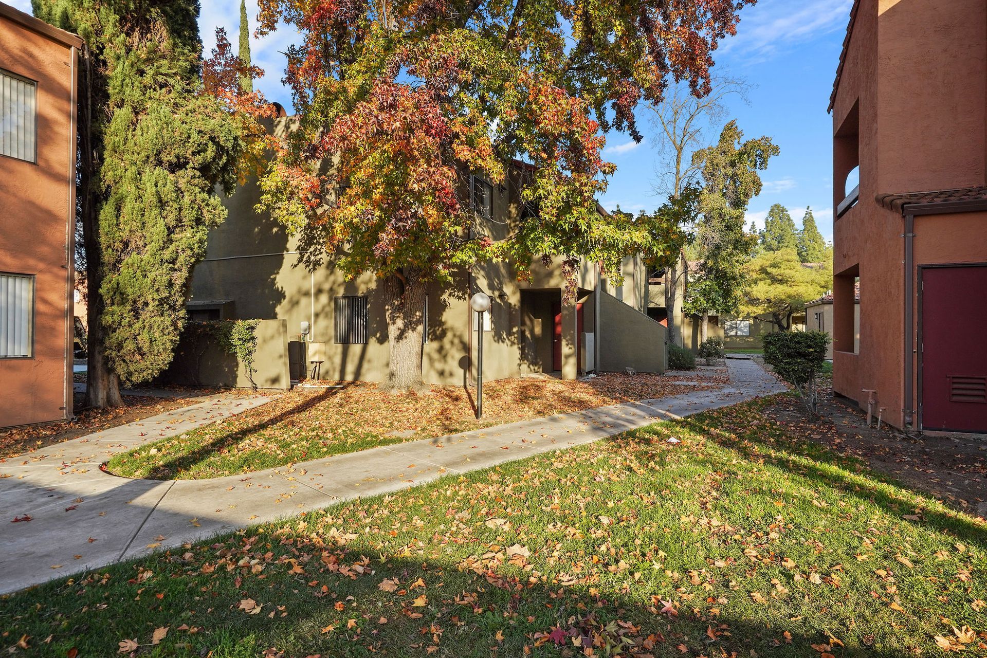 Autumn courtyard with apartment buildings, a concrete walkway, and colorful trees and fallen leaves