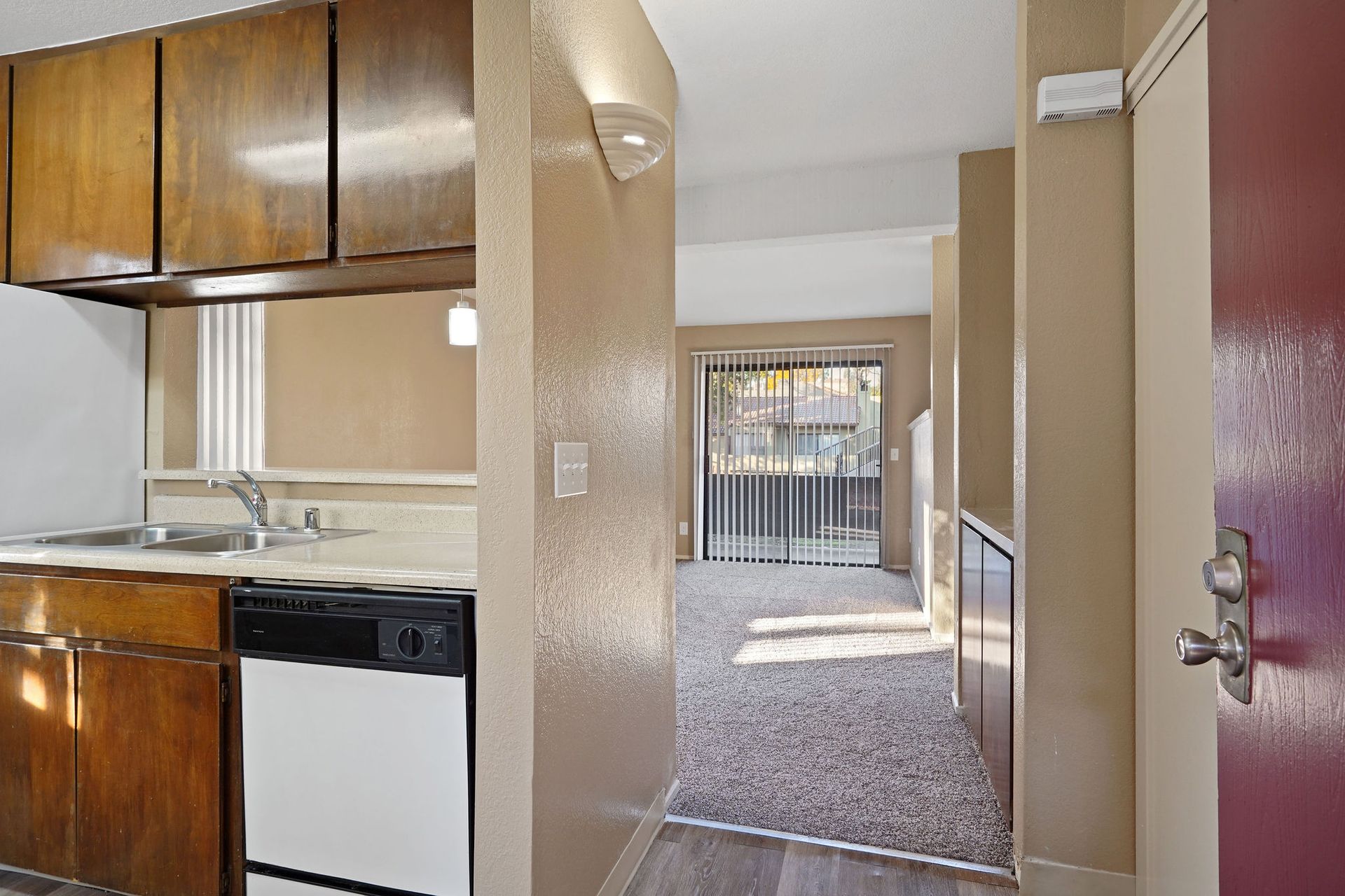 Narrow apartment hallway with kitchen cabinets on the left and a gated entryway ahead.