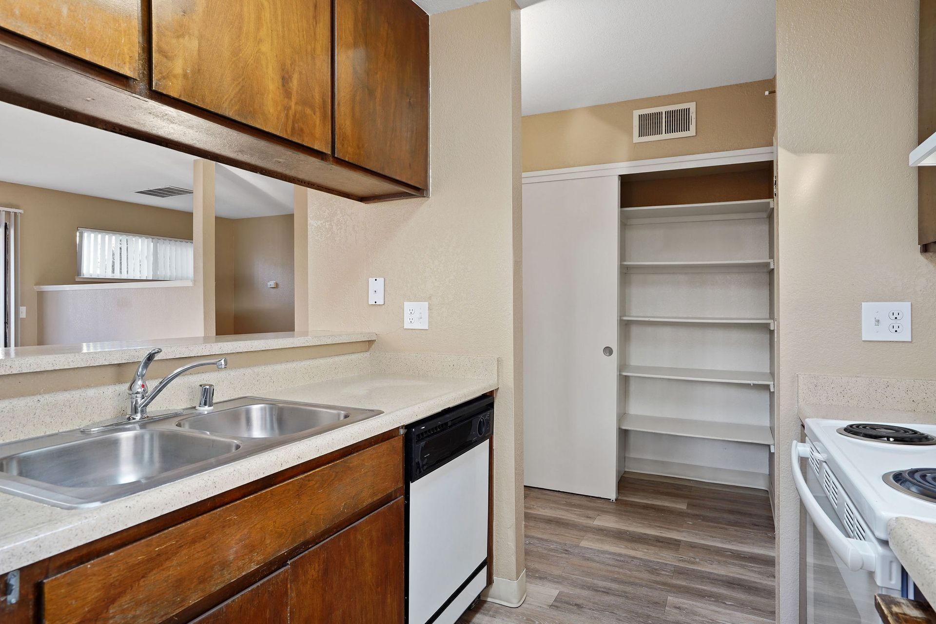 Compact kitchen with tan cabinets, double sink, dishwasher, and open pantry closet.