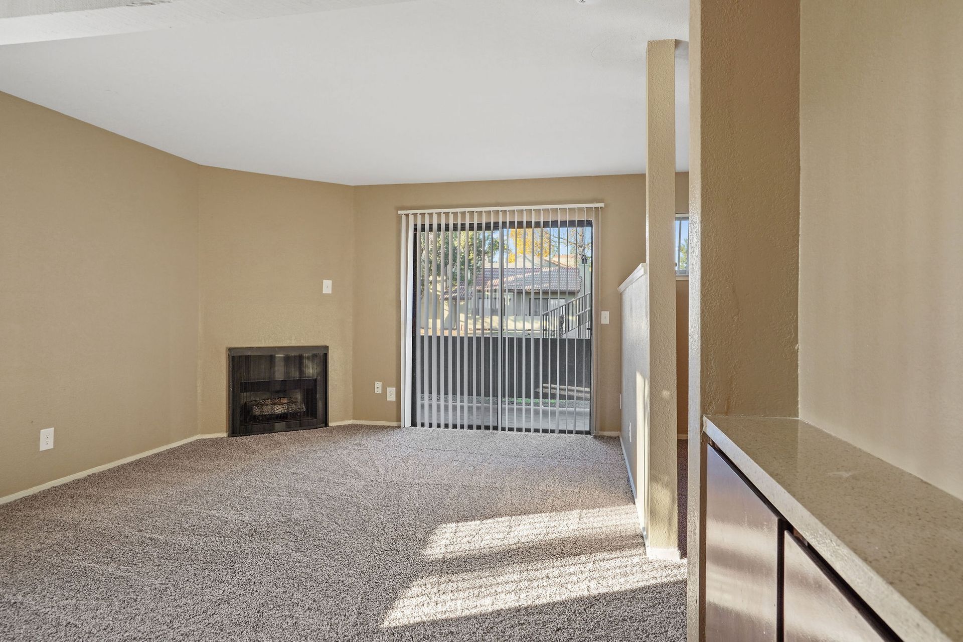 Empty beige living room with carpet, fireplace, and sliding glass doors to a patio