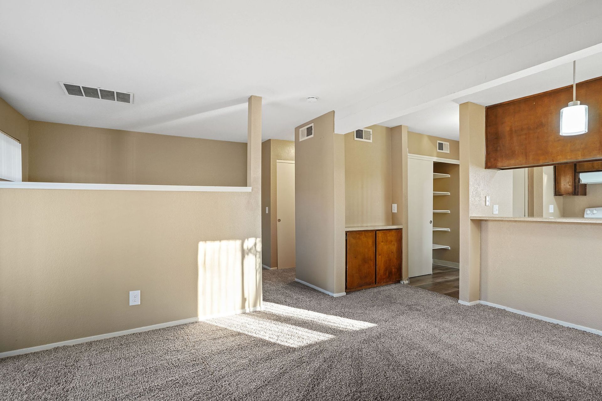 Carpeted living area with beige walls, a partial divider, and a kitchen counter in the background
