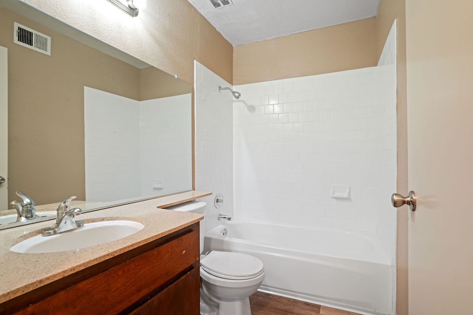 Bathroom with white bathtub and toilet, beige walls, and a wooden vanity with sink and mirror.