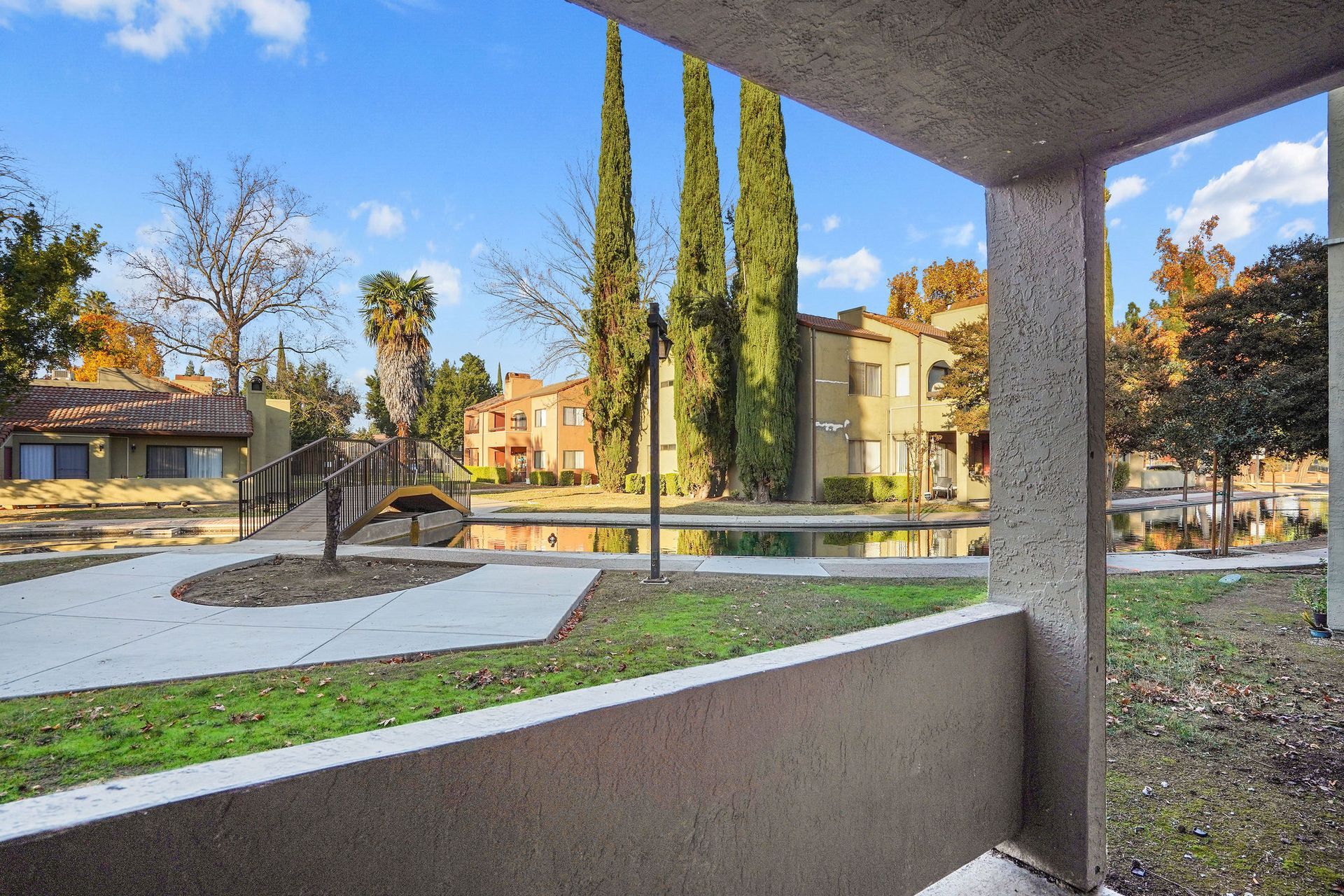 Courtyard view from a covered walkway with green grass, trees, and apartment buildings in the background
