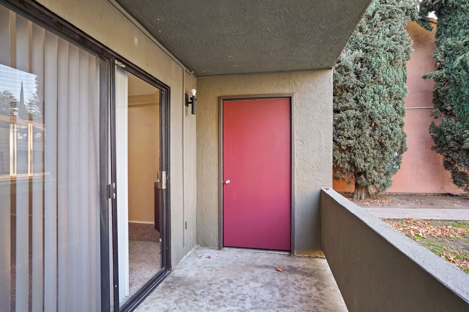 Apartment balcony with a pink door, sliding glass door, and trees outside