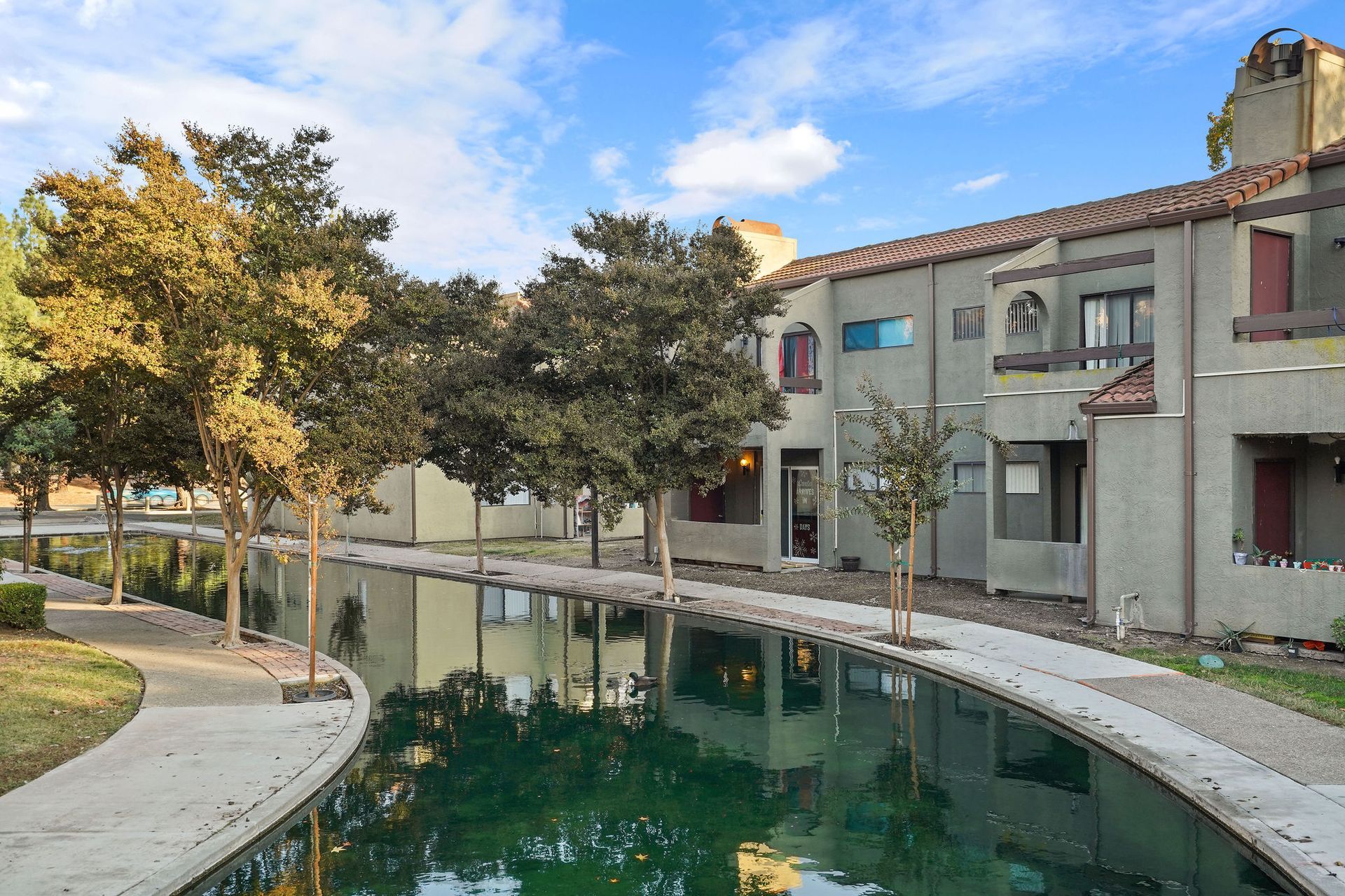 Courtyard with a reflecting pool beside beige apartment buildings and trees at sunset