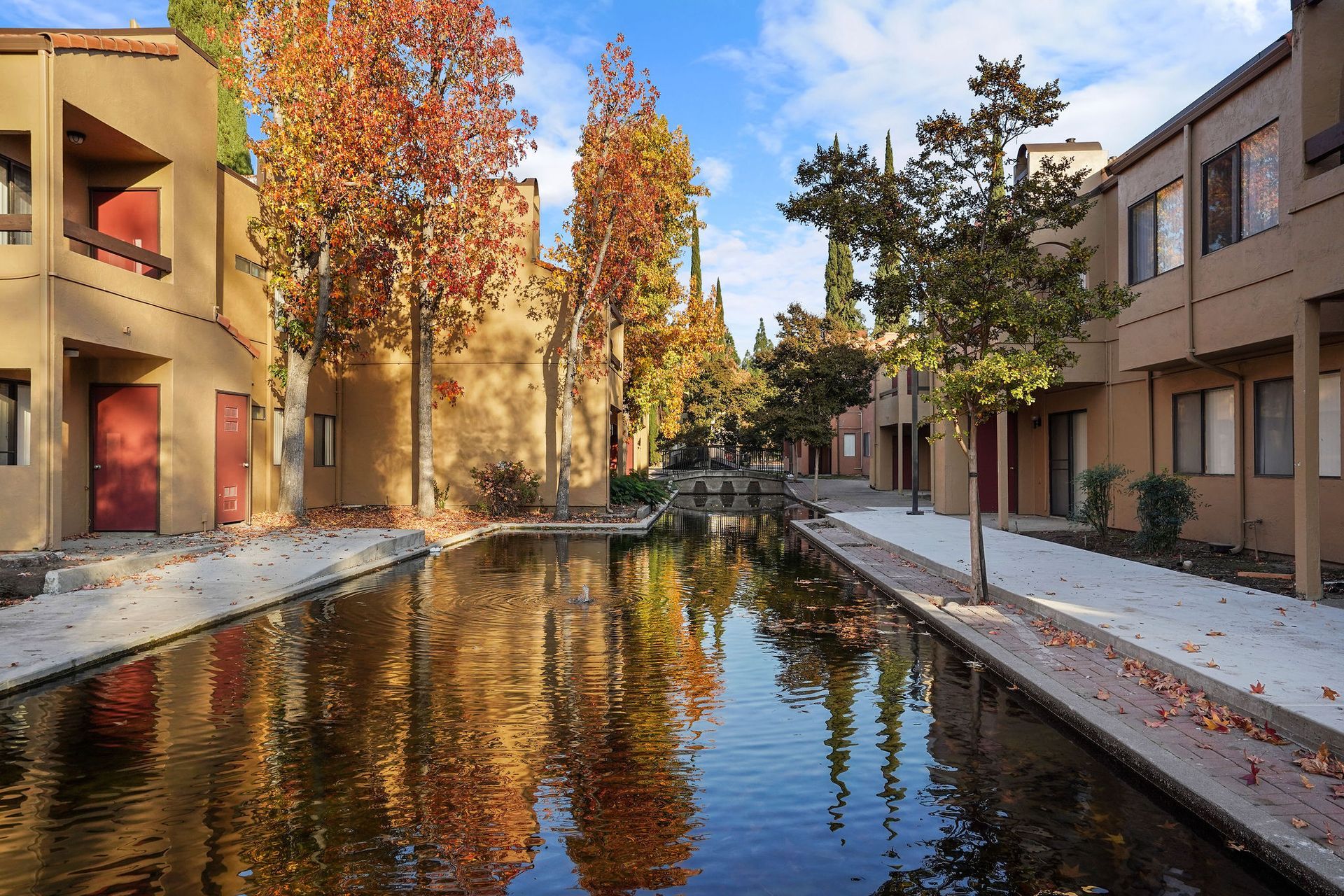 A narrow canal beside modern buildings with autumn trees reflected in calm water