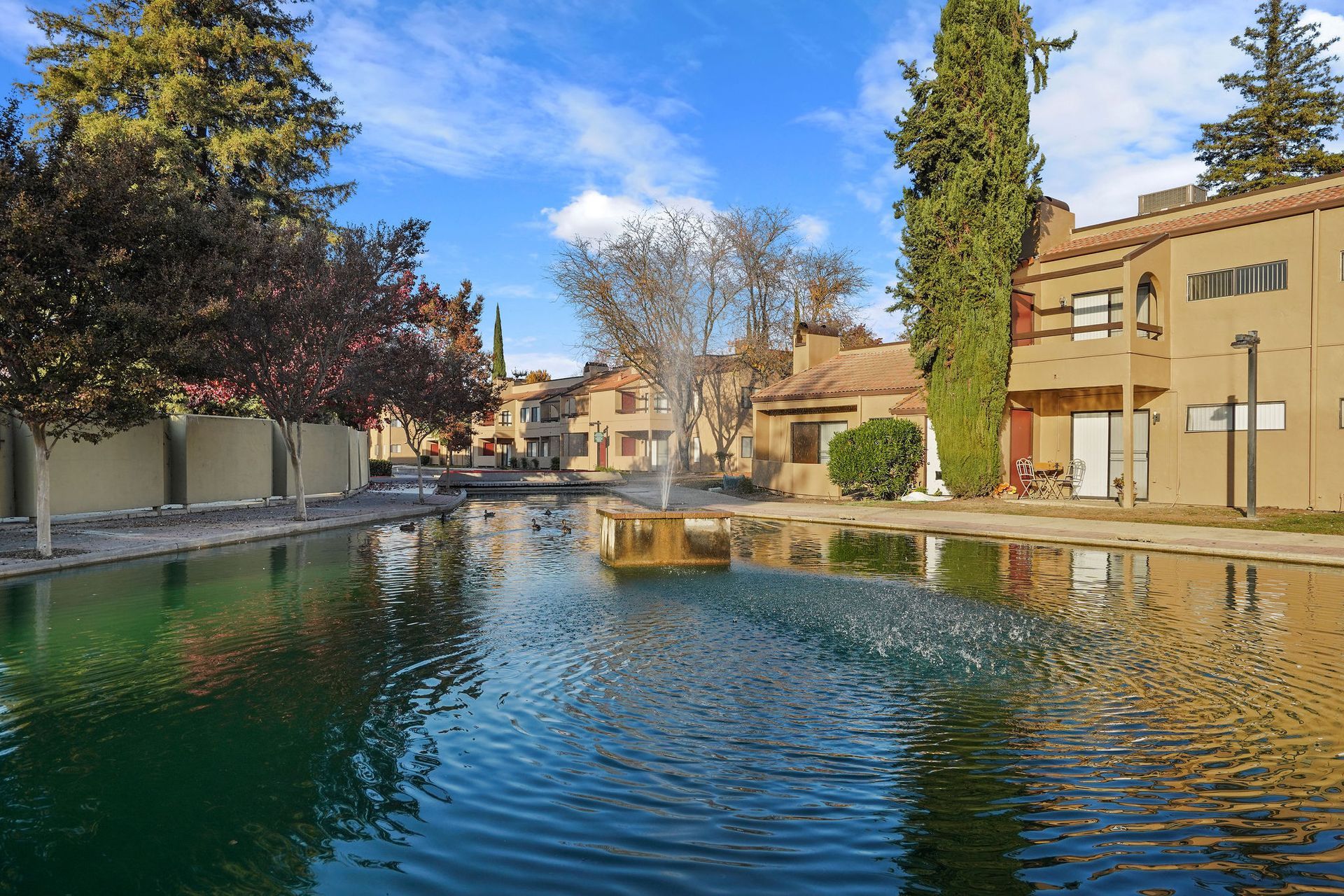Serene courtyard pool reflecting blue sky, with trees and tan buildings on both sides