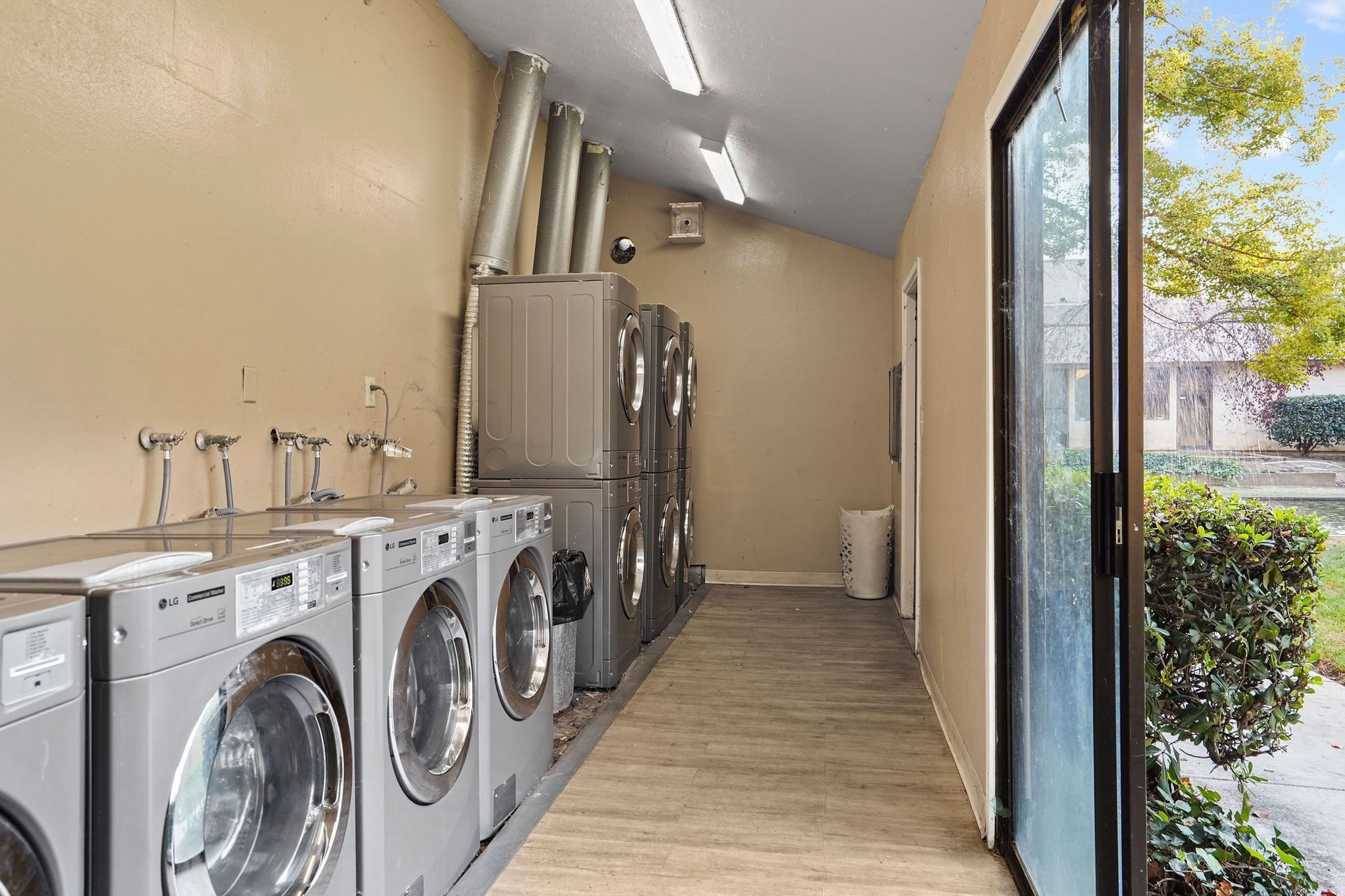 Laundry room with row of washers, stainless steel utility sink, and glass door to outdoor walkway