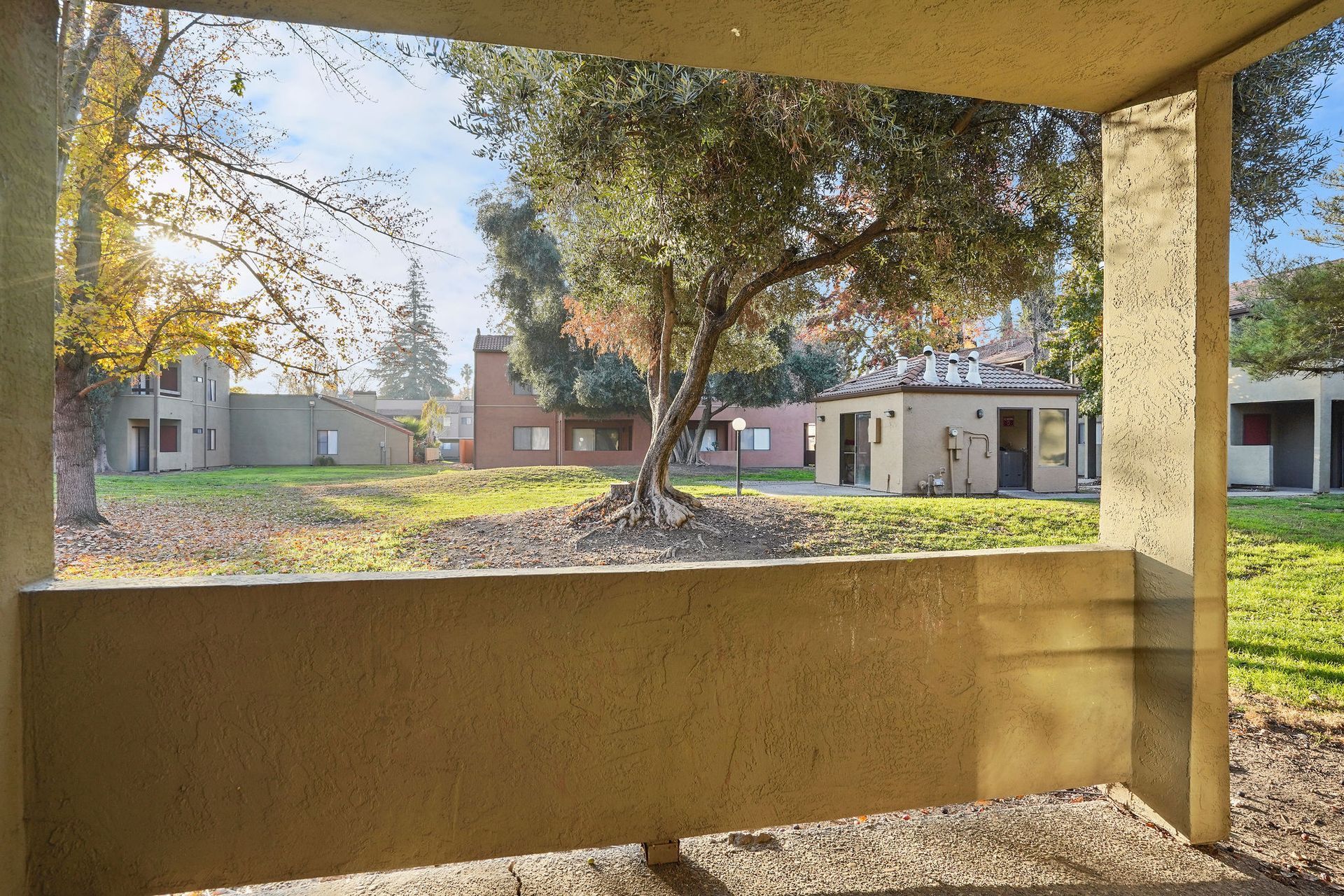 Courtyard view through a shaded porch, with apartment buildings and trees in the background.