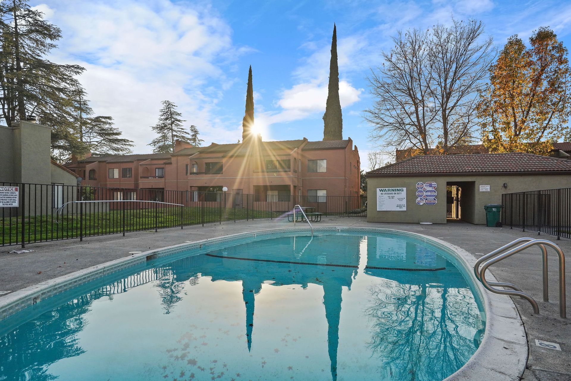 Outdoor swimming pool at sunset with a brick building and tall church spires in the background